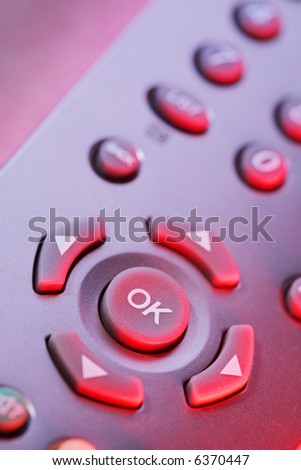 Digital television remote control buttons in red light.