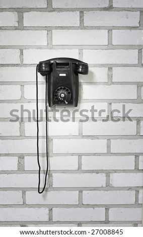 Old black phone hanging on a brick wall