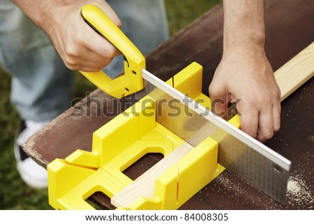 Man cutting a slat of wood using a saw and miter box.
