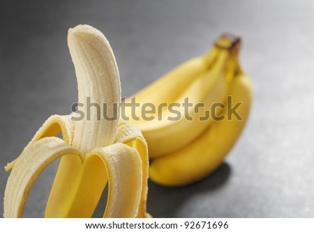 One peeled banana and a bunch of bananas in the background.