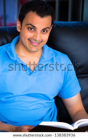 A young happy  student seating on sofa and reading a book on a dusky background