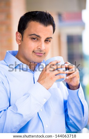 Closeup portrait of young, handsome man standing on his balcony, enjoying a drink, isolated on a city background