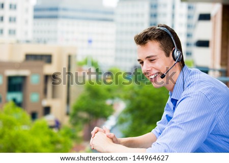 Closeup portrait of customer service representative or call center agent or support or operator with headset on outside balcony, isolated on outside background with trees and buildings
