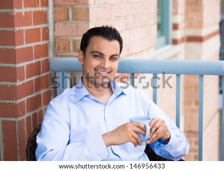 Closeup portrait of handsome guy enjoying drink and sitting on his outside balcony while on vacation