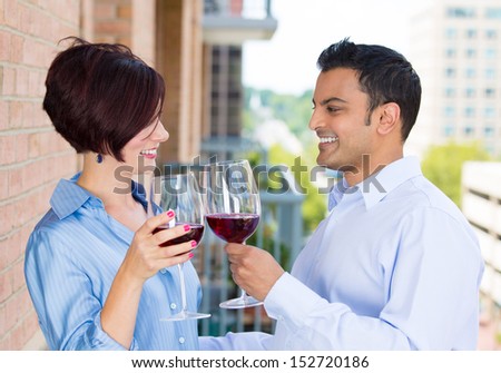 Closeup portrait of man and woman toasting wine on outside balcony, isolated on a city background with trees and buildings