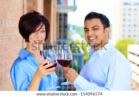 Closeup portrait of man and woman toasting wine on outside balcony, isolated on a city background with trees and buildings