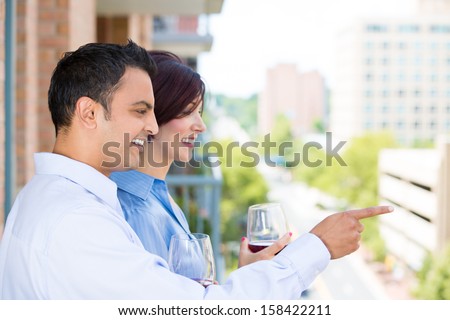 Closeup portrait of man and woman drinking wine and enjoying life on outside balcony, isolated on a city background with trees and buildings