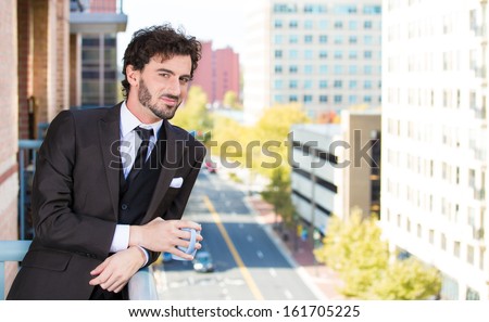 Closeup portrait of good looking smiling, happy businessman, holding a cup of coffee, enjoying a drink, standing on his balcony, isolated on a city background. Urban life style, living of an executive