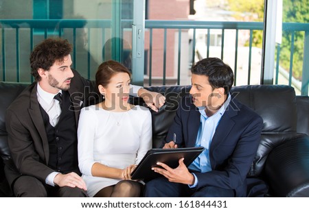 Closeup portrait of agent giving bad news to rich unhappy couple man woman sitting on black couch in house, apartment isolated on city urban background. Financial budget troubles, adverse life events
