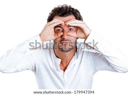Closeup portrait of a young serious curious man peeking through his fingers like binoculars, searching for something, looking to the future at the camera, isolated on a white background. Sign, symbols