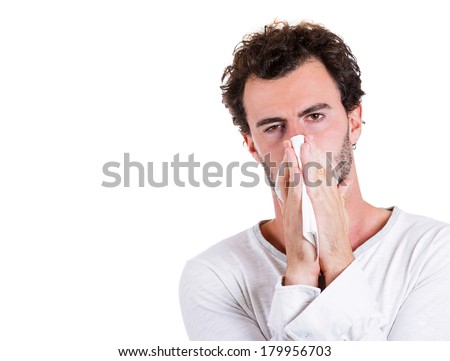 Closeup portrait of sick, ill young man, student, worker with allergy, germs cold, blowing his nose with kleenex, looking miserable, unwell, very sick isolated on white background. Flu season, vaccine