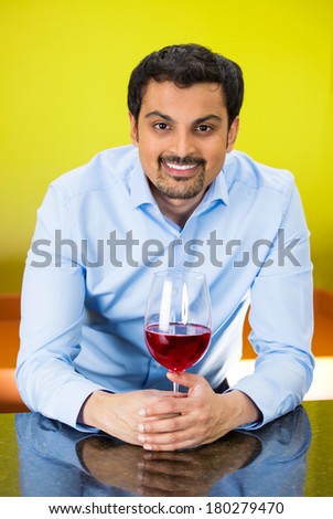 Closeup portrait of young happy, smiling business man with glass of red wine standing at bar, isolated on yellow, green background. Positive human emotion facial expression reaction, leisure, vacation