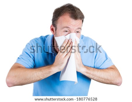Closeup portrait of sick young man student, worker, employee with allergy, germs cold, blowing his nose with kleenex, looking very miserable unwell, isolated on white background. Flu season, vaccine