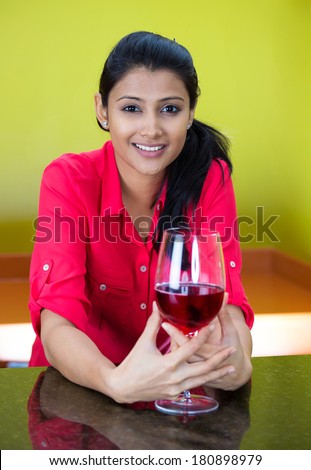 Closeup portrait of young, smiling business woman with glass of red wine standing at bar, isolated on yellow, green background. Positive human emotion facial expression reaction, leisure, vacation