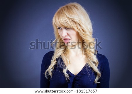 Closeup portrait of young woman disgusted with someone, something, looking to side, sticking out tongue isolated dark blue background. Negative emotion facial expression feelings, reaction, perception