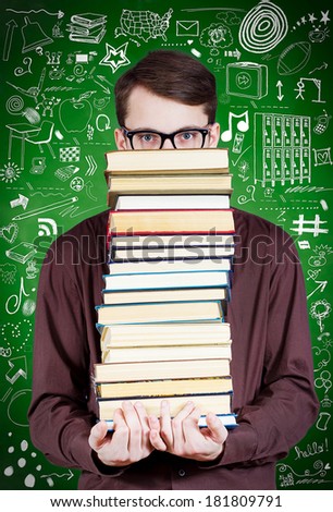 Closeup portrait young man with black eye glasses, student holding huge pile of text books covering his face, looking at you camera, isolated on green background with science, life formulas pictures