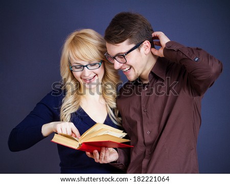 Closeup portrait couple, man, woman, students in glasses, holding red book, smiling, happy, reading funny story, girl pointing at interesting part isolated dark blue, grey background. Positive emotion