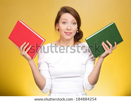 Closeup portrait young serious woman, confused student, holding red and green book in each hand, thinking hard, deciding which one to choose, way to go, isolated yellow background