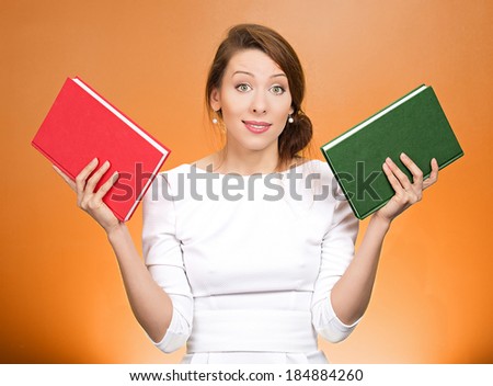 Closeup portrait young serious woman, confused student, holding red and green book in each hand, thinking hard, deciding which one to choose, way to go, isolated orange background