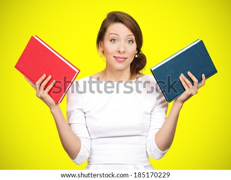 Closeup portrait young serious business woman, confused student holding red, blue book in hands, thinking, deciding which one to choose, way to go, isolated yellow background. Emotions, expressions
