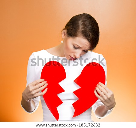 Closeup portrait young, troubled, sad, confused woman, holding broken heart in hands, about to cry, isolated orange background. Negative human emotions, facial expression, feelings, attitude, reaction