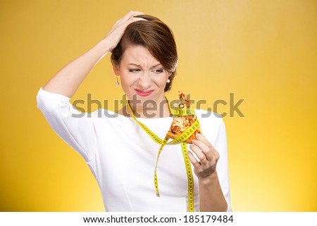 Closeup portrait sad, young, confused woman holding, looking at fatty pizza with measuring tape around, trying to withstand, resist temptation to eat it isolated yellow background.  Facial expression