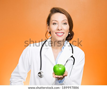 Closeup portrait, confident happy health care professional, doctor, nurse in lab coat, offering you fruit, isolated orange background. Apple a day keeps doctor away concept. Nutrition, healthy diet