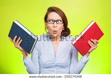 Closeup portrait, young business woman, confused student holding red, brown books in hands, frustrated, deciding which one to choose, way to go, isolated green background. Emotions, expressions