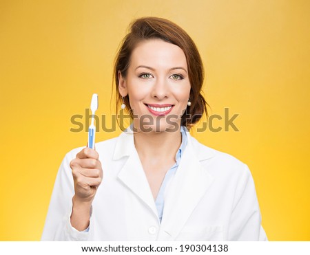 Closeup portrait young, happy, smiling health care professional, female dentist, holding manual toothbrush, isolated yellow background. Oral dental health, hygiene, disease prevention. Positive face