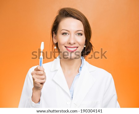 Closeup portrait young, happy, smiling health care professional, female dentist, holding manual toothbrush, isolated orange background. Oral dental health, hygiene, disease prevention. Positive face