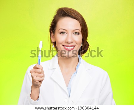 Closeup portrait young, happy, smiling health care professional, female dentist, holding manual toothbrush, isolated green background. Oral dental health, hygiene, disease prevention. Positive face
