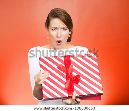 Closeup portrait young woman holding opening gift box, displeased, shocked angry disgusted with what received, isolated red background. Negative human emotions, facial expressions, feeling, reaction