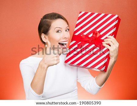 Closeup portrait happy, excited young woman about to open, unwrap red birthday gift box, giving thumbs up isolated red background. Positive emotions, facial expressions, feelings, attitude, reaction