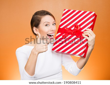 Closeup portrait happy, excited young woman about to open, unwrap red birthday gift box, giving thumbs up isolated orange background. Positive emotions, facial expression, feelings, attitude, reaction
