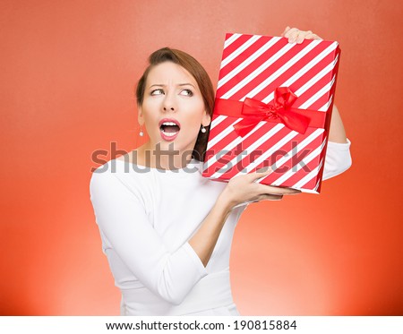 Closeup portrait happy, excited young woman about to unwrap red birthday gift box, wondering what is inside isolated red background. Positive emotion, facial expressions, feelings, attitude, reaction