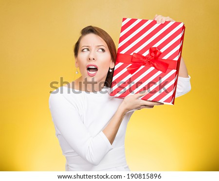Closeup portrait happy, excited young woman about to unwrap red birthday gift box, wondering what is inside isolated yellow background. Positive emotion, facial expression, feeling, attitude, reaction