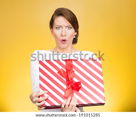 Closeup portrait young woman holding opening gift box, displeased, shocked angry, disgusted with what received, isolated yellow background. Negative human emotion, facial expression, feeling, reaction