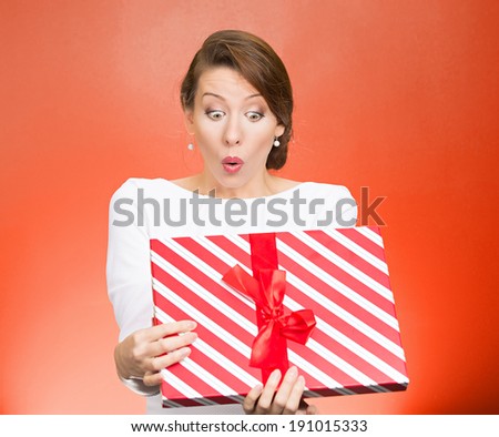 Closeup portrait young woman holding opening gift box, displeased, shocked angry, disgusted with what received, isolated red background. Negative human emotion, facial expression, feeling, reaction