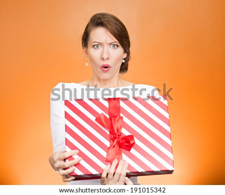 Closeup portrait young woman holding opening gift box, displeased, shocked angry, disgusted with what received, isolated orange background. Negative human emotion, facial expression, feeling, reaction
