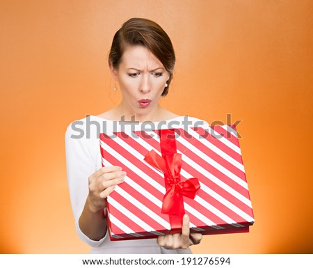 Closeup portrait young funny woman holding opening gift box, surprised, shocked with unexpected present received, isolated orange background. Sudden human emotion, facial expression, feeling, reaction