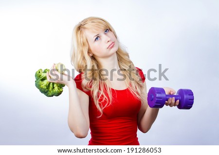 Closeup portrait, unhappy, annoyed, grumpy, displeased, young woman, girl with disgust on face, holding green broccoli, dumbbell in hands, questioning healthy life style recommendations. Expression