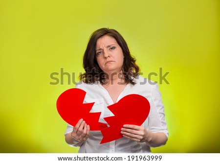 Closeup portrait middle aged, troubled, sad, confused woman, holding broken heart in hands, thinking, isolated green background. Negative human emotion, facial expression, feelings, life reaction