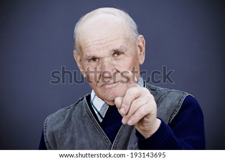 Closeup portrait serious looking, senior mature, elderly man pointing, at you with index finger, gesture, isolated dark, grey background. Negative human emotions, facial expressions, feelings, symbols