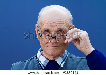 Closeup portrait senior serious mature man with glasses looking at you camera gesture skeptically isolated blue background. Negative human emotion facial expression, feeling, body language, perception