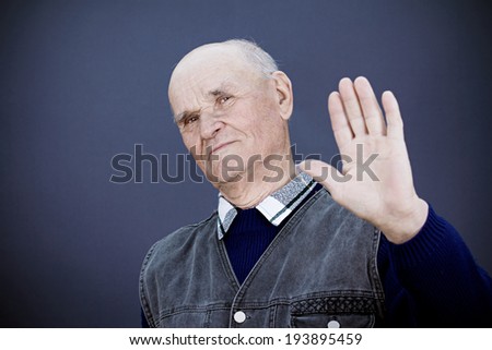 Closeup portrait senior mature grumpy man with bad attitude giving talk to hand gesture with palm outward, isolated blue, black background. Negative emotion, facial expression feelings, body language