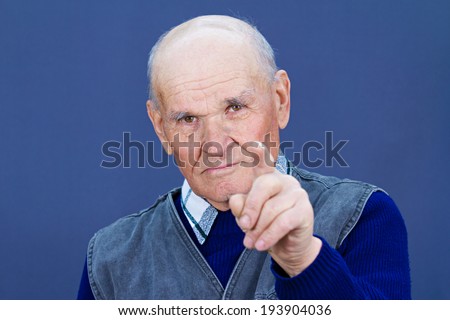 Closeup portrait serious looking, senior mature, elderly man pointing, at you with index finger, gesture, isolated blue background. Negative human emotions, facial expressions, feelings, symbols