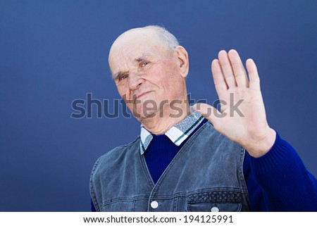 Closeup portrait senior mature grumpy man with bad attitude giving talk to hand gesture with palm outward isolated blue background. Negative emotion facial expression feeling, body language perception