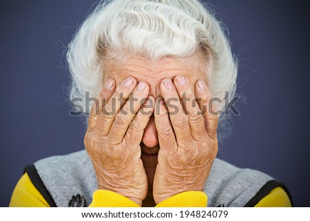Closeup portrait sad depressed, stressed, thoughtful, senior, old woman, gloomy, worried,  covering her face, isolated blue background. Human face expressions, emotion, feelings, reaction, attitude