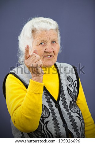 Closeup portrait serious looking, senior mature, elderly woman pointing, at you with index finger, gesture, isolated blue background. Negative human emotions, facial expressions, feelings, symbols