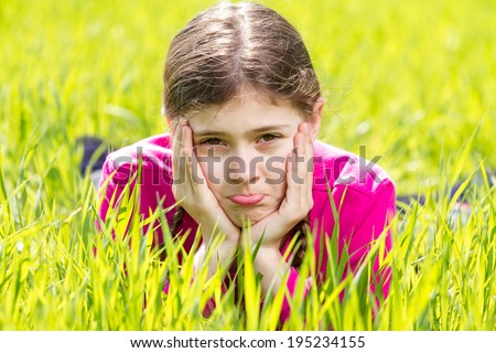 Closeup portrait sweet little, cute, funny looking girl, making faces, unhappy about something, laying in green grass isolated outdoors background. Childhood, emotion, facial expression, body language